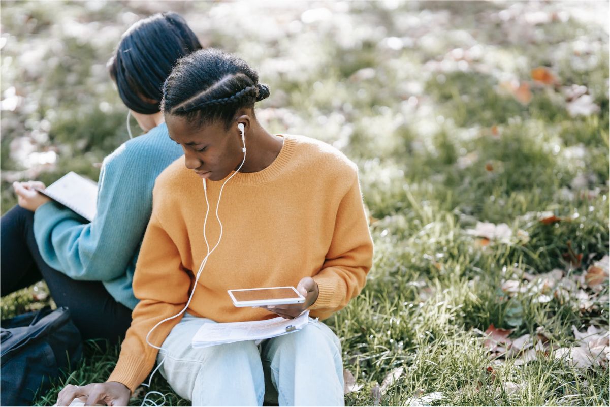 two girls sitting in a yard, listening to a podcast