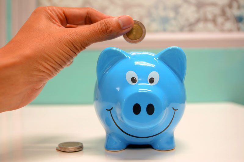 Someone is putting a coin into a blue piggy bank